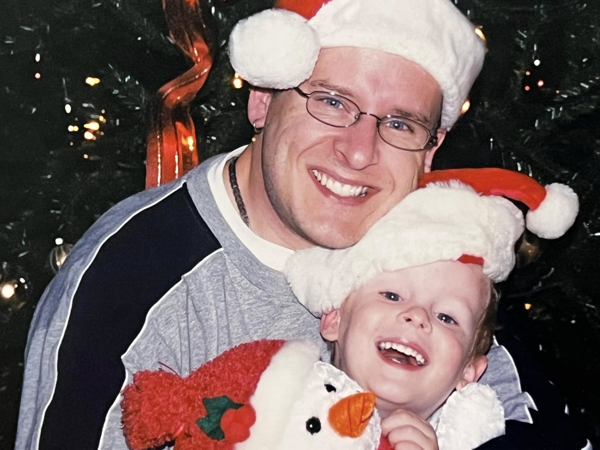 Jim McMahel and his young son in Santa hats in front of a Christmas tree
